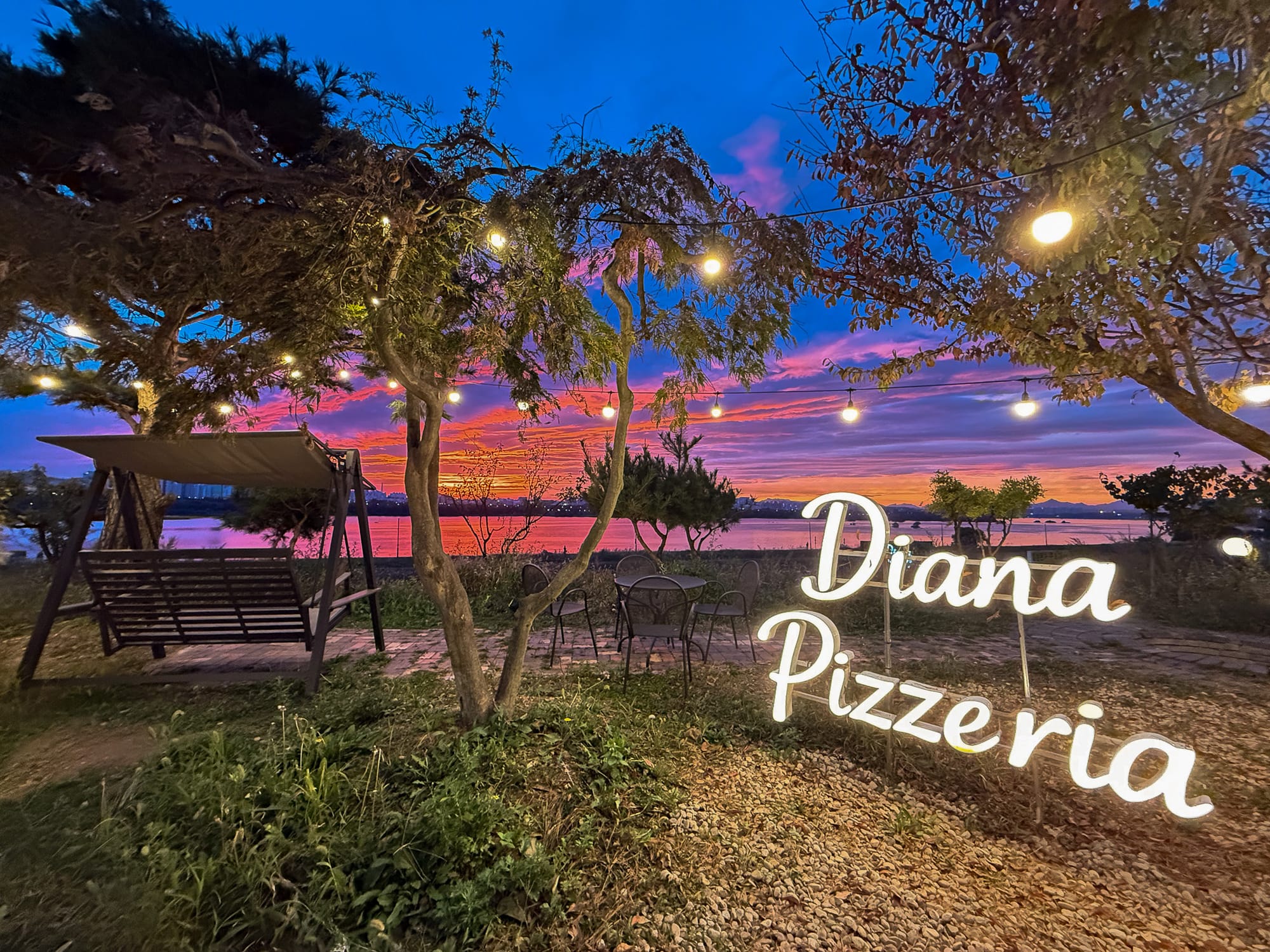 전구가 켜진 정원과 Diana Pizzeria 사인